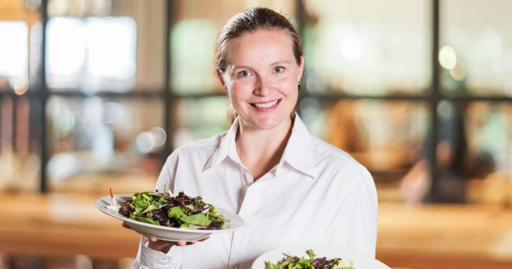 Waitress serving a portion of salad and smiling friendly.