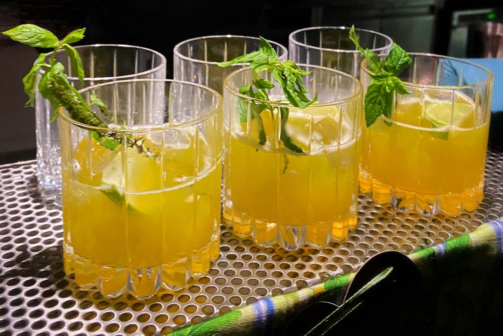 MIntunoksalla koristeltuja keltaisia juomia laseissa peräkkäin baaritisillä.